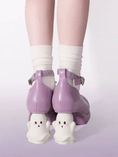 the image shows the back view of a person's legs from the knees down. they are wearing white socks and purple platform shoes with a chunky heel. each shoe has a small, smiling ghost figure attached to the heel. the ghost figures are white with pink cheeks and black eyes. the background is a solid lavender color.