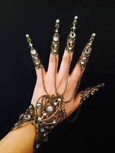 a hand is adorned with an ornate set of vintagestyle jewelry, including finger armor on the fingers, a linked chain and finger bracelet, and a larger bracelet around the wrist, all featuring intricate designs and embedded crystals. the backdrop is black.