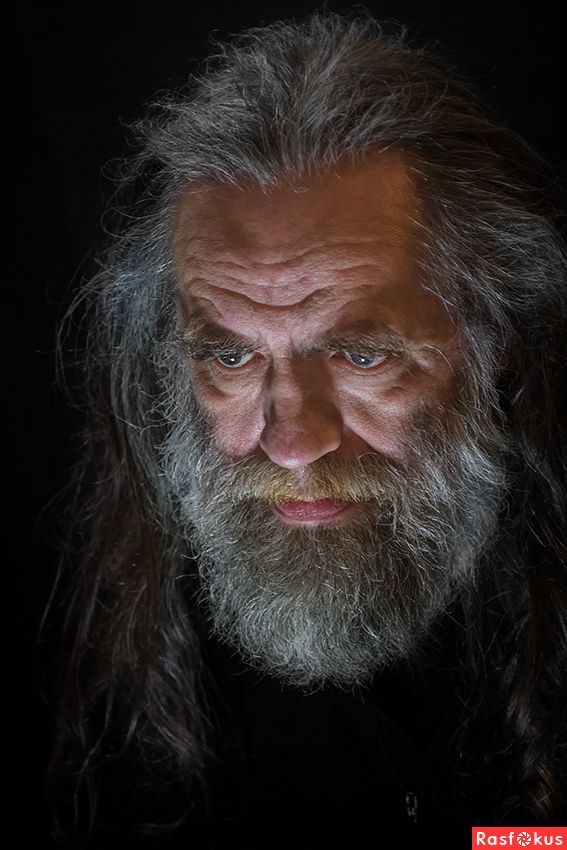 a closeup portrait of an older man with long gray hair and a full gray beard. his face is weathered with deep lines, and he has a serious, almost intense expression. the lighting is dramatic, highlighting his features against a dark background.