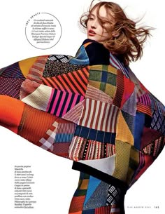 a woman in a colorful patchwork sweater looks at the camera during a photoshoot. her hair is tousled and she wears a serious expression.
