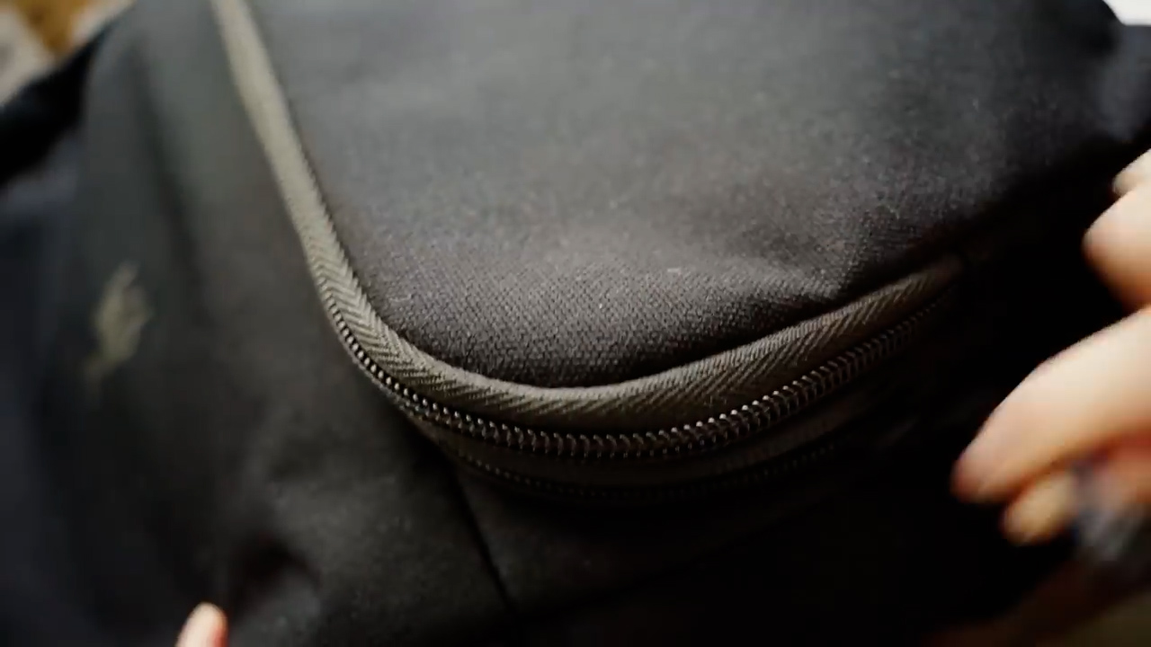 a closeup shot of a black backpack with a zipper. the backpack is made of a durable fabric and has a sleek design. the zipper is black and has a metal pull.