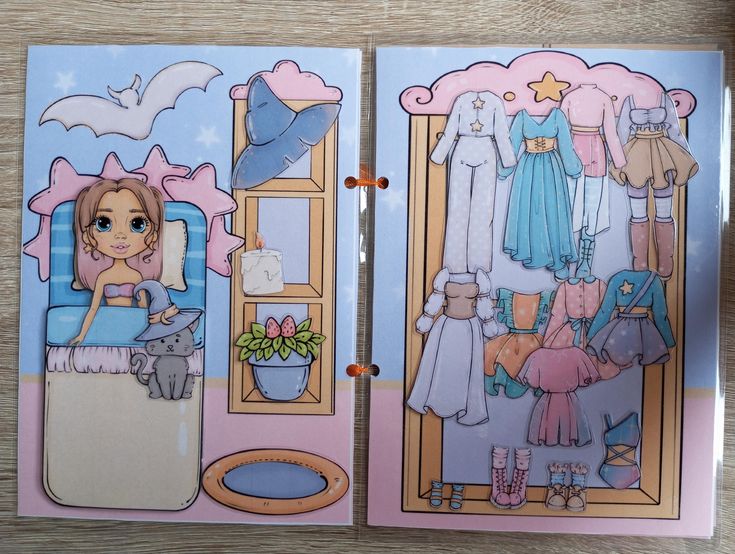 the image shows an open paper doll book. on the left page is a girl in bed with a cat wearing a witch's hat. there is a window with a candle and a flowerpot on the side. a bat is flying above the bed. on the right page is a wardrobe with a collection of paper doll clothes, including dresses, pajamas, and shoes.