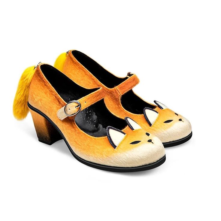 the image shows a pair of whimsical women's shoes designed to resemble foxes. the shoes are orange with white fox face details on the toe, black and white ears, and a fuzzy yellow tail attached to the heel. they are mary jane style heels with a strap across the foot. the shoes are set against a plain white background.