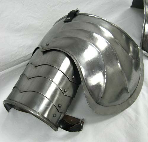 a closeup shot of a gleaming steel pauldron, a piece of medieval armor designed to protect the shoulder. the pauldron is made of polished metal with prominent ridges for added strength and defense. it has a curved shape to fit snugly over the shoulder and upper arm, with leather straps and buckles for fastening. the image is taken indoors with bright, artificial lighting that highlights the metallic sheen and craftsmanship of the armor piece.