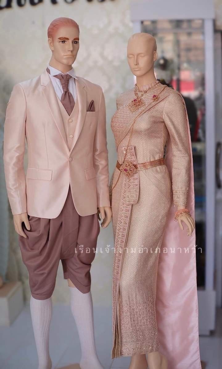 a bride and groom in traditional thai wedding attire. the bride is wearing a beautiful pink and gold dress, while the groom is wearing a matching suit. the couple looks very happy and in love.