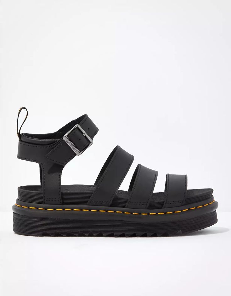 the image shows a pair of black dr. martens platform sandals. the sandals have a thick, chunky sole with distinctive yellow stitching. they feature a black leather upper with several straps across the foot and an adjustable buckle around the ankle. the background is a plain white.