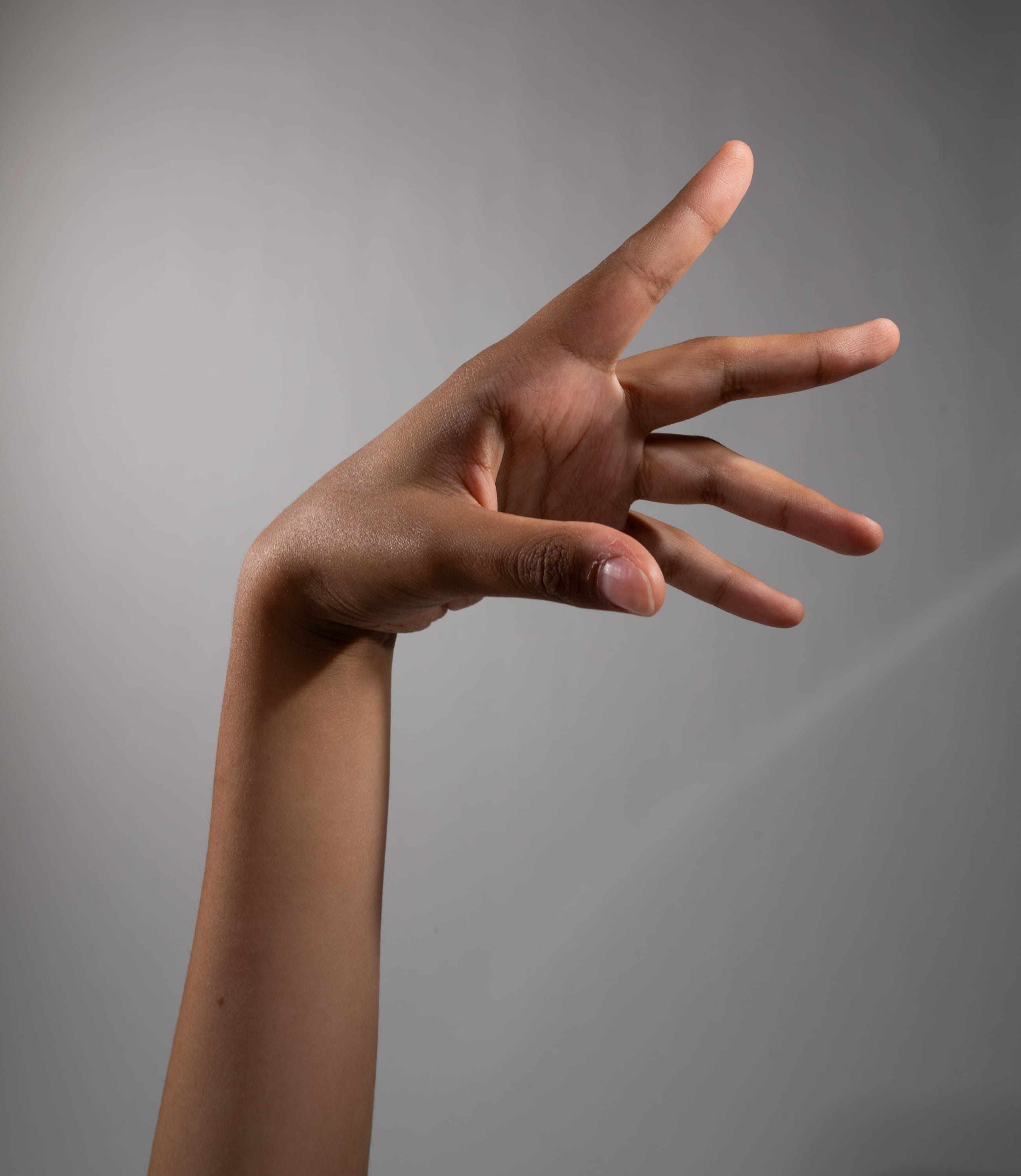 a closeup side view of a hand gesturing against a light grey background. the hand is outstretched with the fingers spread apart. the lighting is bright, illuminating the details of the skin and the contours of the hand.