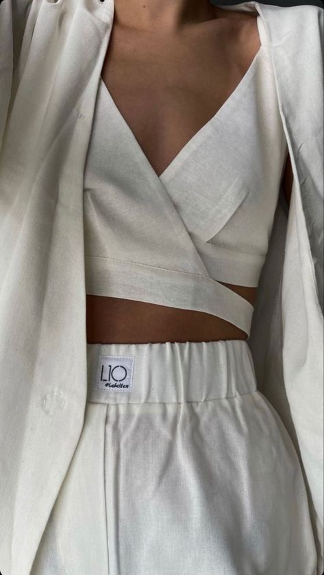 a woman is wearing a white linen suit, which includes a blazer, a crop top, and matching pants. the suit is styled in a minimalist and chic way, reflecting a summer fashion aesthetic. the soft, natural lighting enhances the clean and fresh look of the outfit.