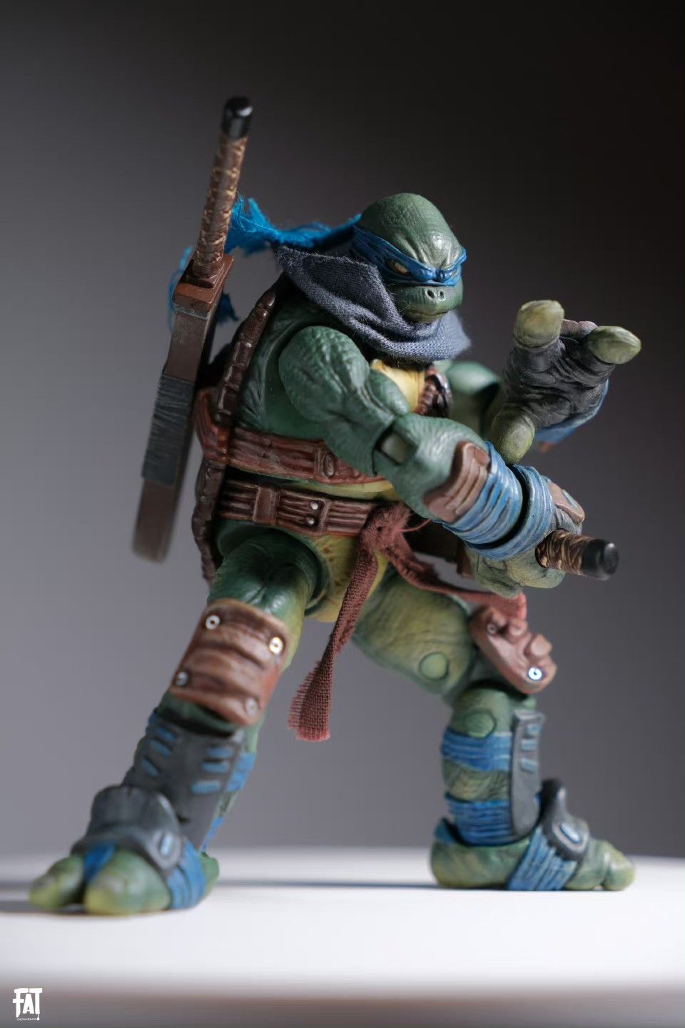 a teenage mutant ninja turtles leonardo action figure stands on a white surface. he is in a fighting pose, holding a sword, and wearing his signature blue bandana.