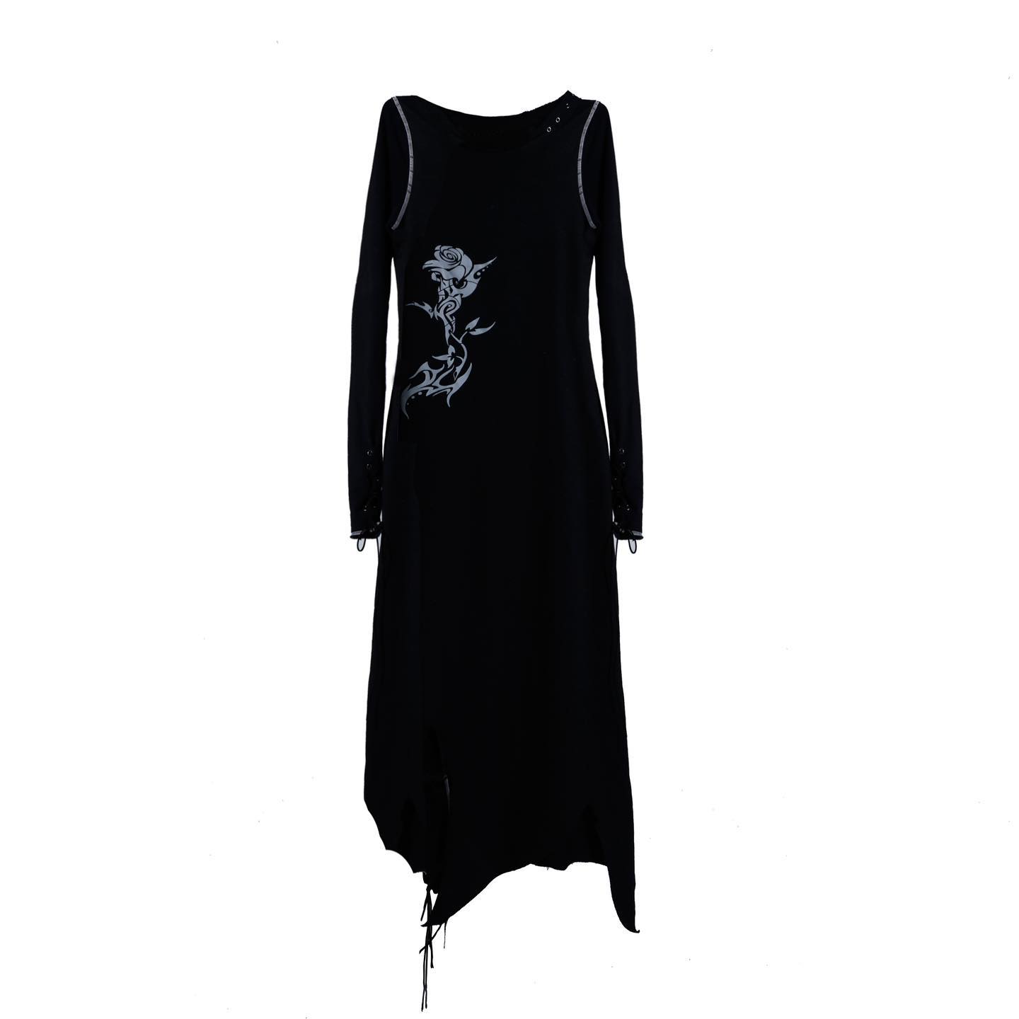 the image shows a black, longsleeved dress with an asymmetrical hemline. the dress has a rose and tribalinspired design on the side, and laceup details on the sleeves and hem. the fabric appears to be a soft knit. the dress hangs on a plain white background.