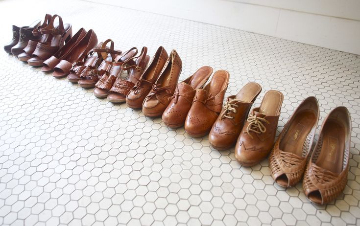 a line of brown shoes, including sandals, pumps, and clogs, are lined up on a white, hexagonal tile floor.