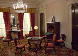 the image shows the interior of a wellfurnished room, likely a historic home. the space is designed in a classic style with rich, dark wood furniture, patterned carpets, and heavy drapes. a round table sits in the center, illuminated by a tiffanystyle lamp. additional chairs are arranged around the room, inviting conversation and relaxation. the room exudes a sense of history and elegance.