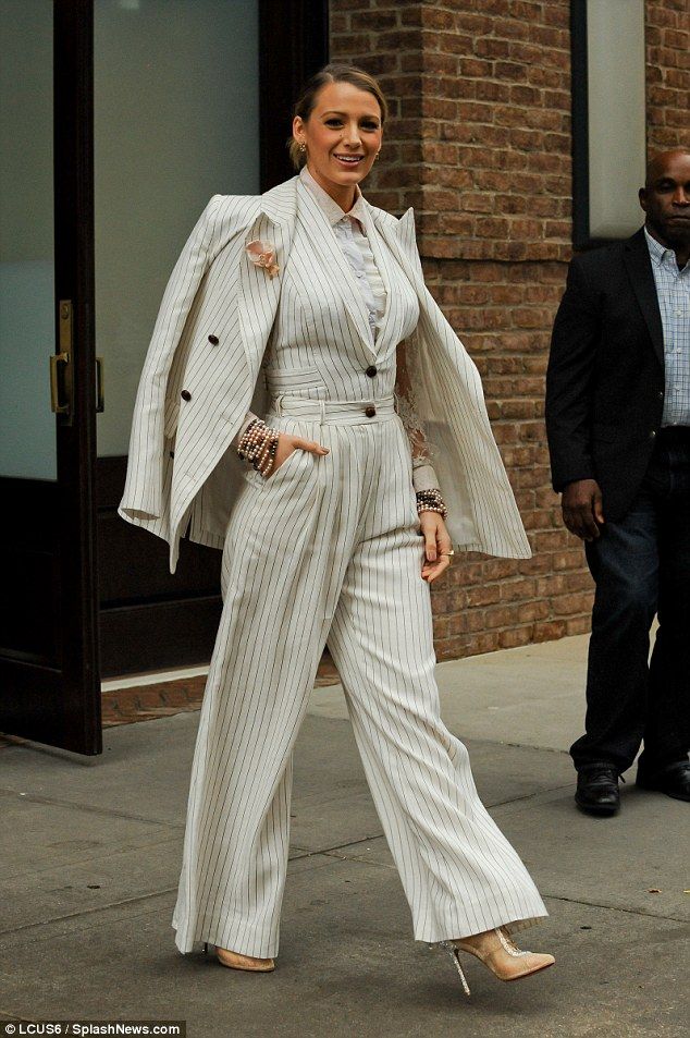 blake lively is photographed on the streets of the city, wearing a white pinstripe suit with a white shirt and shoes. she is walking down the sidewalk while smiling at the camera.