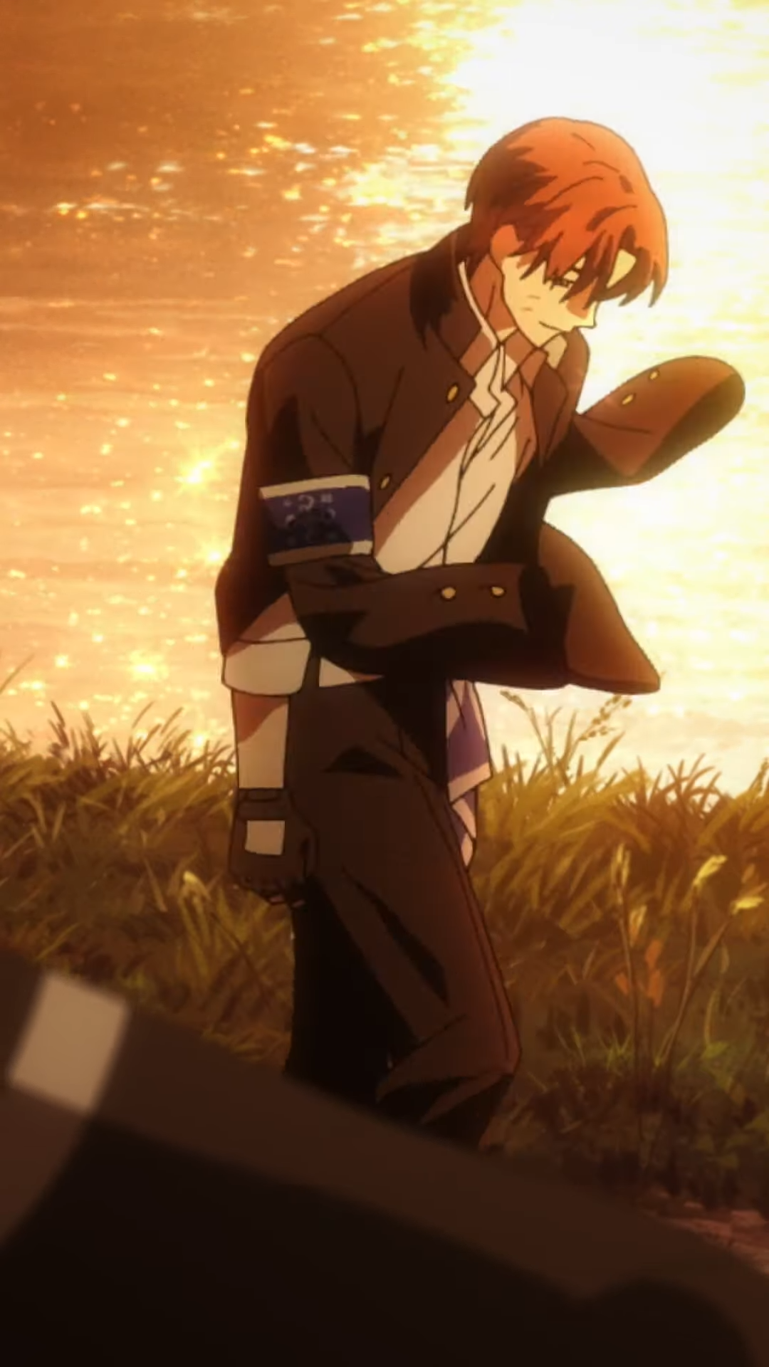 an anime character with short red hair and brown eyes, wearing a white shirt, an undone blue tie, and a black blazer with a blue armband walks away from the camera towards the right. the sun is setting in the background, casting a warm glow on the water and grass. the overall palette is warm and golden.