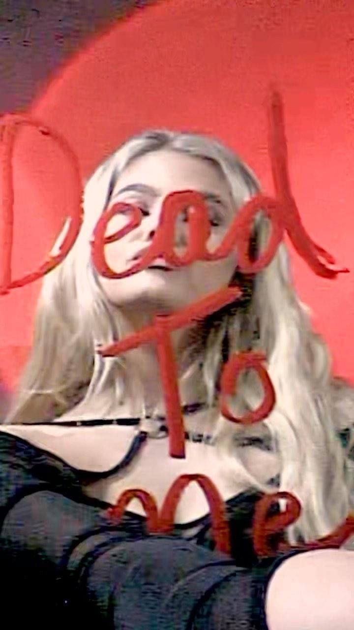 a woman with blonde hair poses behind a pane of glass with the words "dead to me" written in red on the glass.