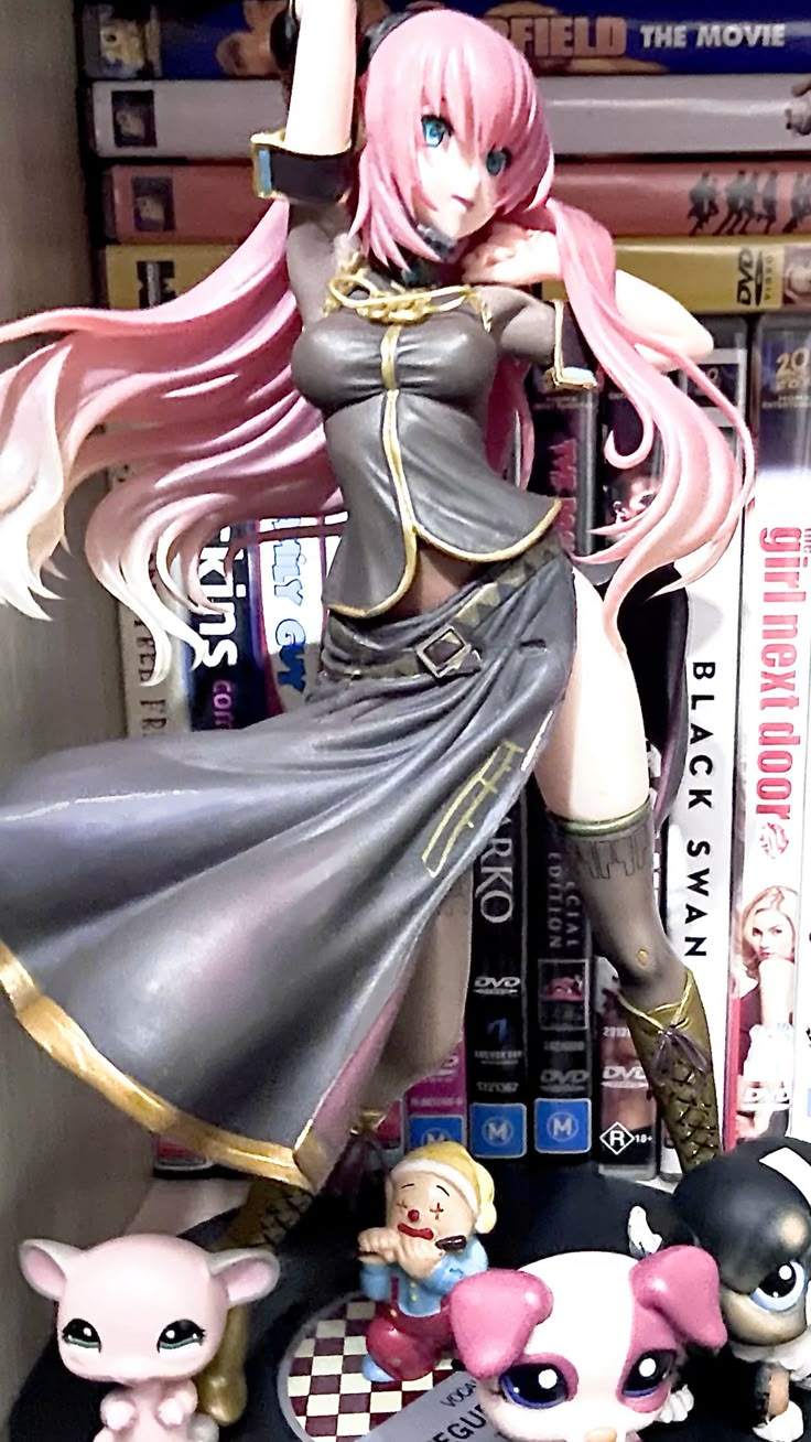 this image shows a luka anime figurine, along with several other figurines and movies on a shelf. the luka figurine is in the center of the frame, with her flowing pink hair and blue eyes drawing attention. she is wearing a gray outfit. behind her are various dvds and movies, adding depth to the image. in the foreground, there are smaller figurines, including a clown and lps pets, adding a playful touch to the scene.