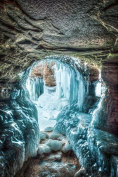 the image shows a frozen cave with large icicles hanging from the ceiling and walls. there is a path of ice and snow leading through the cave, with the rocky ceiling visible above. the scene evokes a sense of cold and natural beauty.