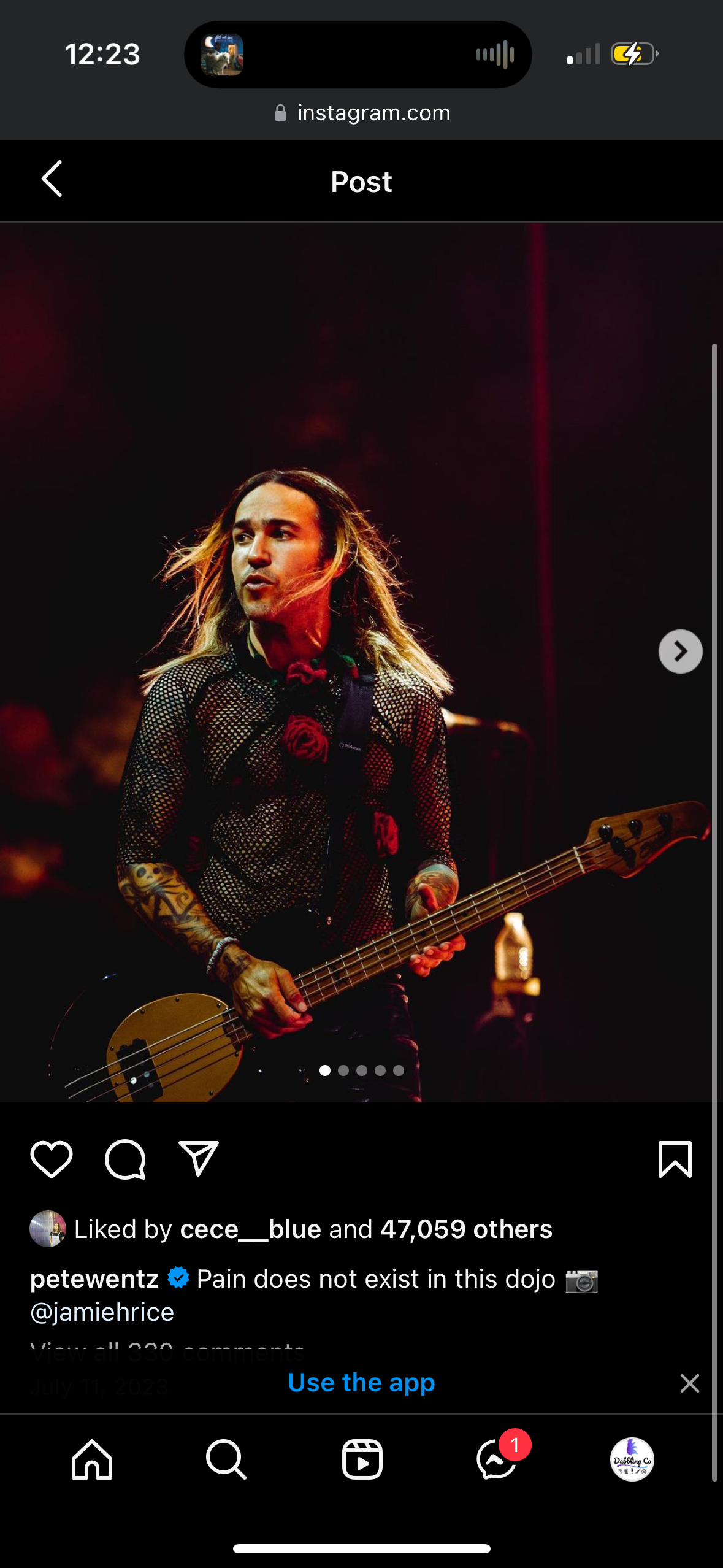 pete wentz, the bassist for the band fall out boy, is playing bass guitar on a stage. he's wearing a black mesh shirt, and has long black hair. there is a microphone stand visible on the stage. it appears that he's performing at a concert or music festival.