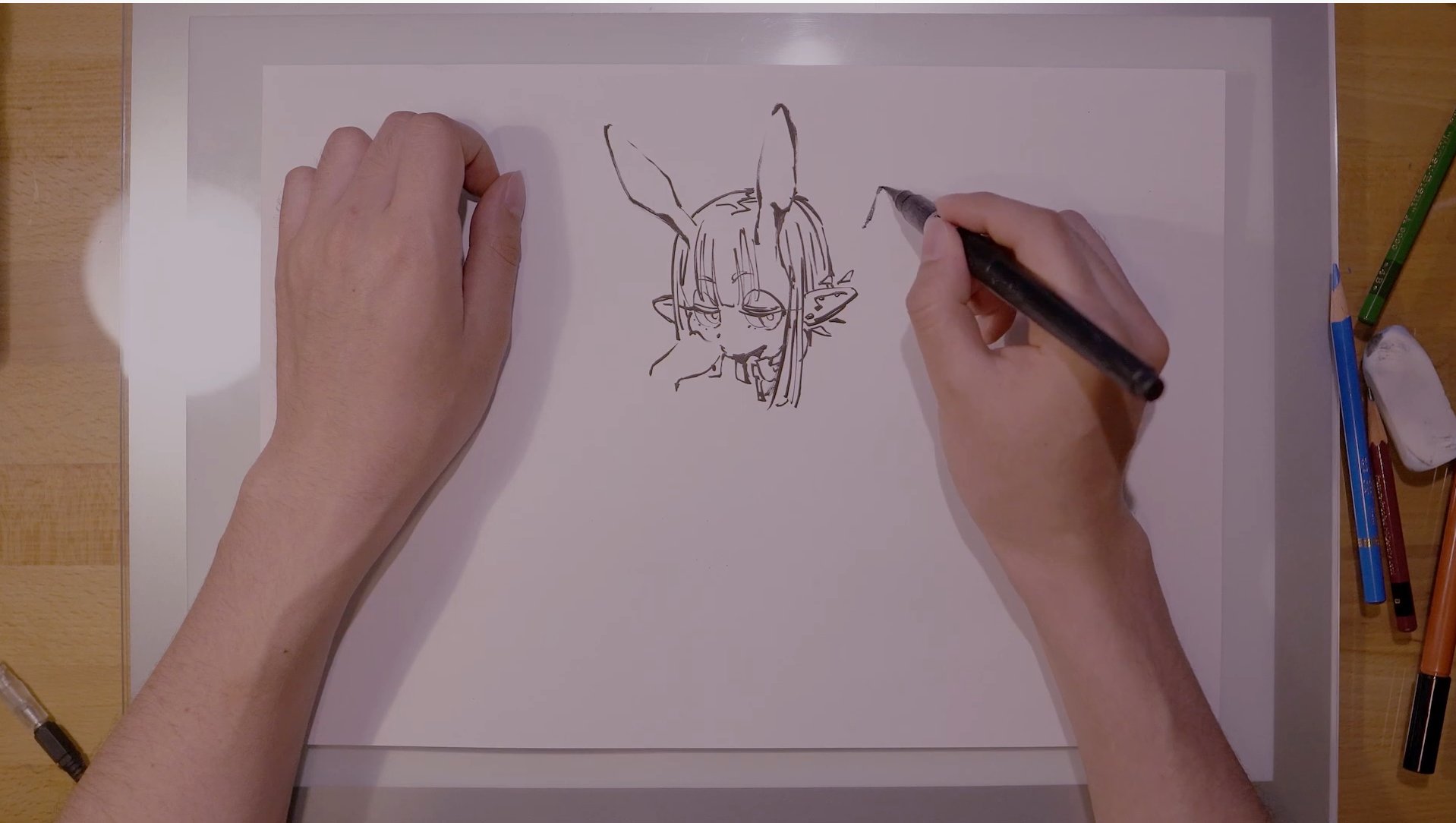 an overhead shot captures an artist's hands in the midst of creating a character sketch on white paper. the drawing depicts a female anime character with bunny ears, her expression partially obscured.  the artist wields a black pen, the tool of their craft, bringing the illustration to life with each stroke. the surrounding table hints at a dedicated workspace, scattered with art supplies like pencils and erasers.