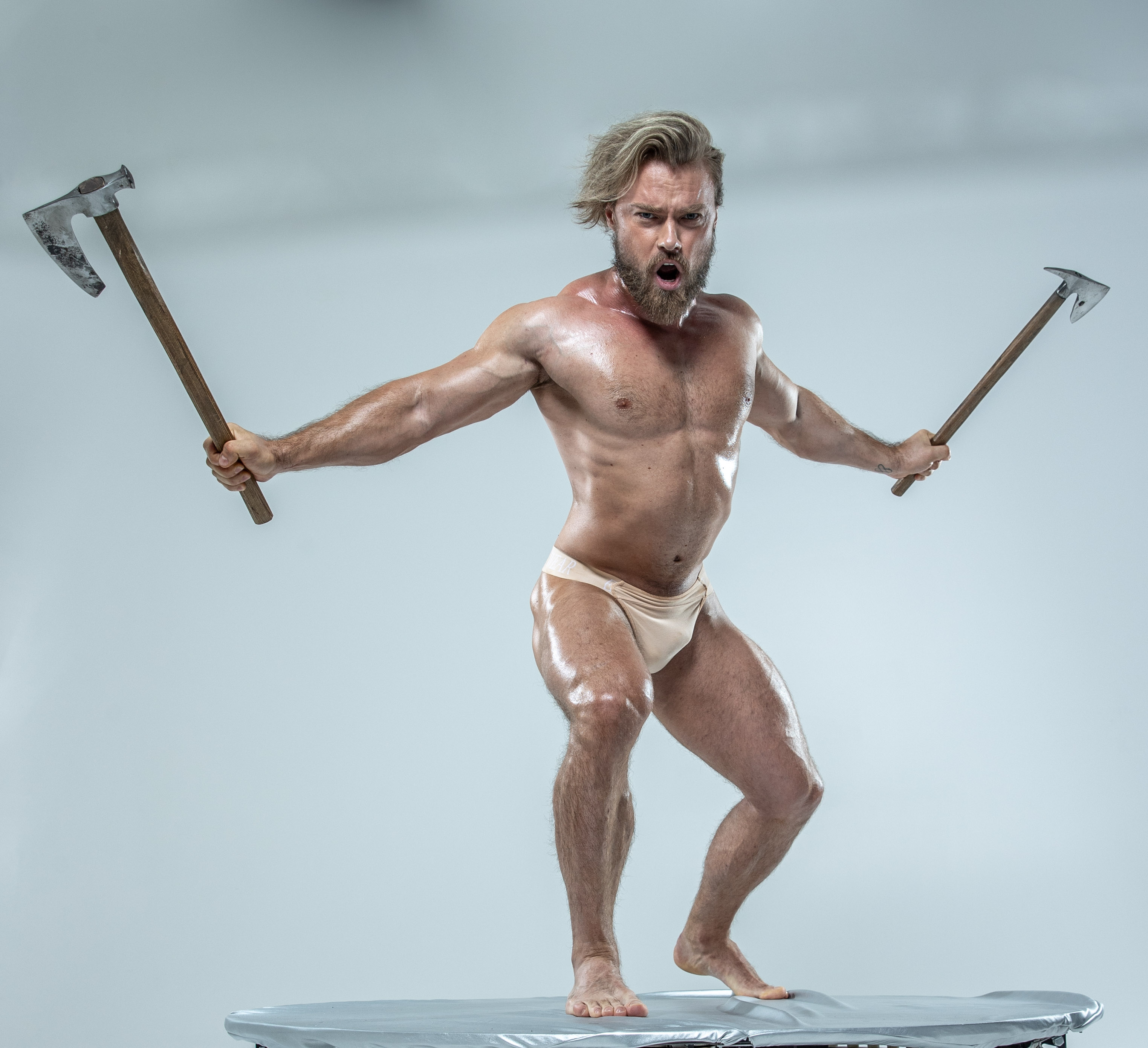 a muscular man with an angry expression stands on a small round platform, dual wielding axes. the background is solid white.