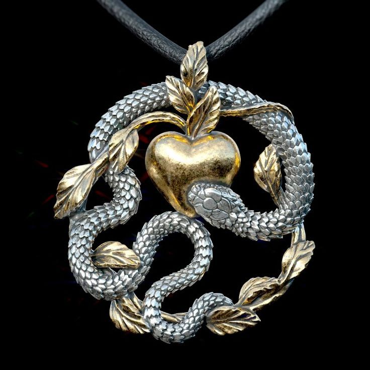 a closeup shot of a pendant featuring a snake coiled around a golden apple, with leaves accenting the design. the snake is silver in color and appears to be biting or guarding the apple. the pendant hangs from a black cord against a black background.