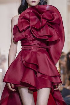 a beautiful model showcases an elegant red dress with ruffles and a highlow hemline on a runway. the dress is a statement piece, with its intricate details and glamorous design. the model's confident pose and stunning looks add to the overall appeal of the ensemble. this is a highfashion piece that would be perfect for a special occasion or evening event.