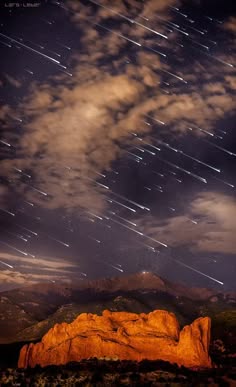 a stunning view of a meteor shower over the garden of the gods in colorado. the night sky is filled with shooting stars, streaking across the dark blue canvas. the red rock formations of the garden of the gods stand out against the night sky, creating a dramatic and aweinspiring scene. the clouds add a sense of depth and mystery to the image.