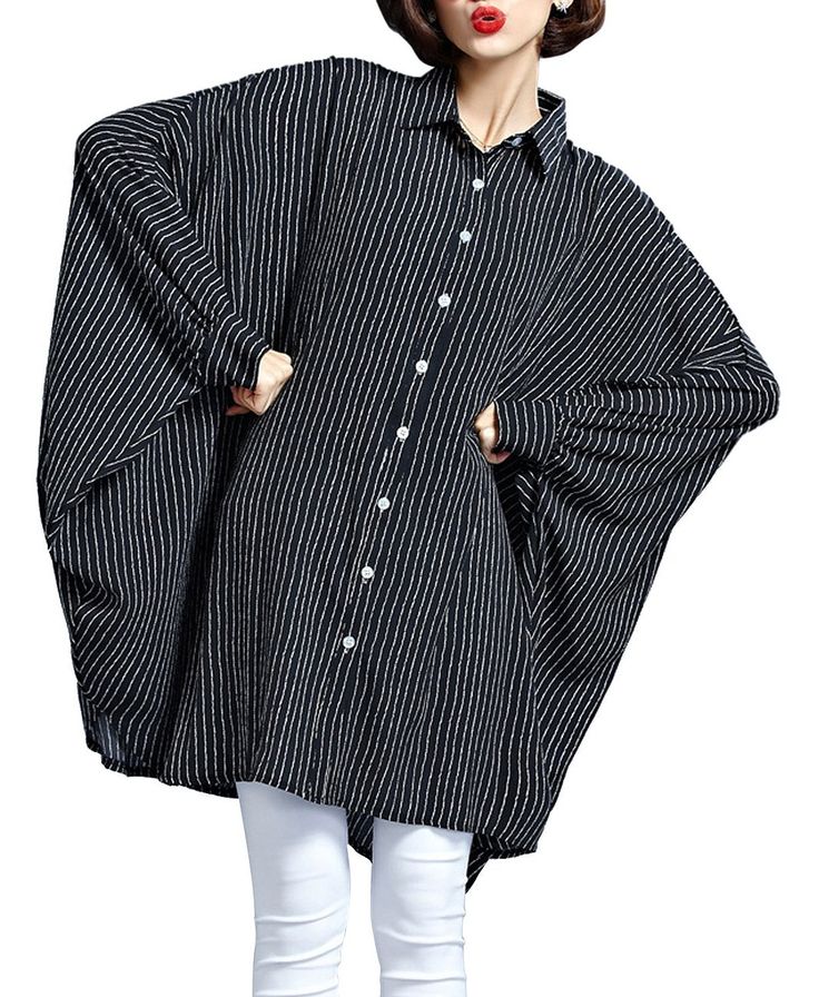 a woman is wearing a black and white striped oversized buttondown shirt with long sleeves and white pants. she is standing with her hands on her hips.
