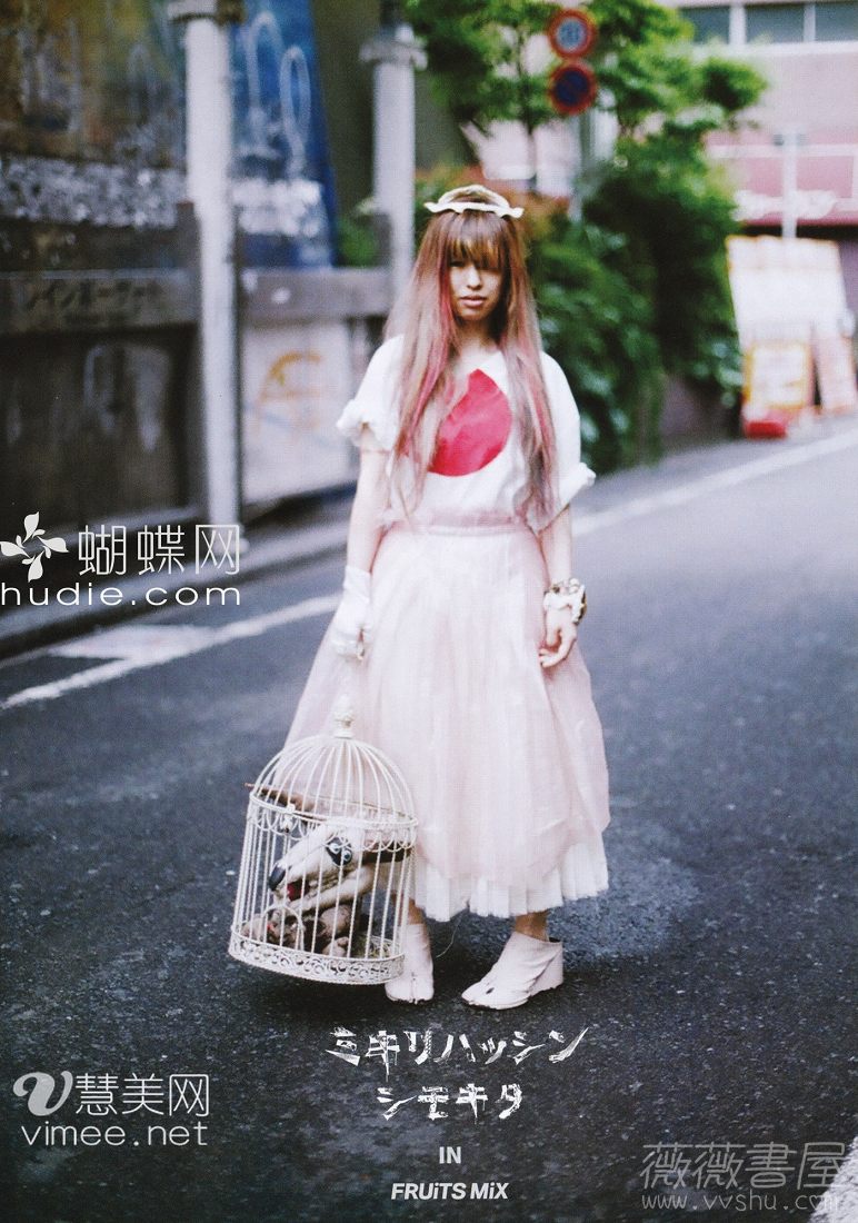young woman in harajuku street style poses on a city street. she has bleached blonde hair with pink tips, and wears a white top with a red circle design, a tiered pink tulle skirt, and white shoes. she is carrying a large white bird cage with a stuffed animal inside. the image includes watermarks for several websites.