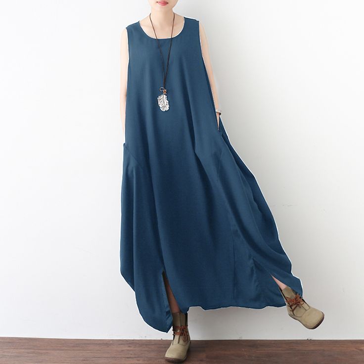 a woman stands in front of a white wall, wearing a sleeveless maxi dress. the dress is a solid dark blue color, and it appears to be made of a soft, flowing fabric. she is also wearing a pair of anklehigh tan boots with laces, and a long necklace with a pendant. the style of the dress and boots suggests a casual, bohemian look. the woman's expression is neutral and she is looking directly at the viewer.