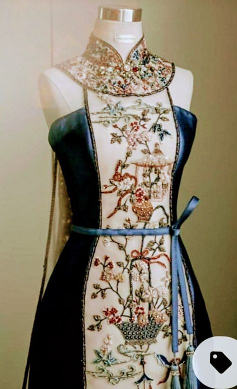 a closeup view of a beautiful embroidered dress on a mannequin. the dress features a mandarin collar, a blue satin bodice, and a sheer skirt with intricate embroidery of floral motifs and birds. the embroidery is done in a variety of colors, including gold, beige, and brown. a blue ribbon is tied around the waist. the overall look is elegant and sophisticated.