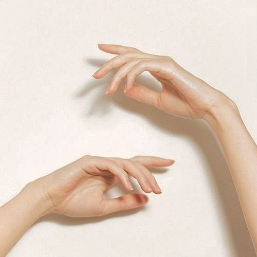 the image shows two pale, smooth hands against an ivory colored background. the hands are positioned gracefully with slightly bent fingers. the skin is clean and appears wellmaintained. light falls on the hands creating soft shadows.