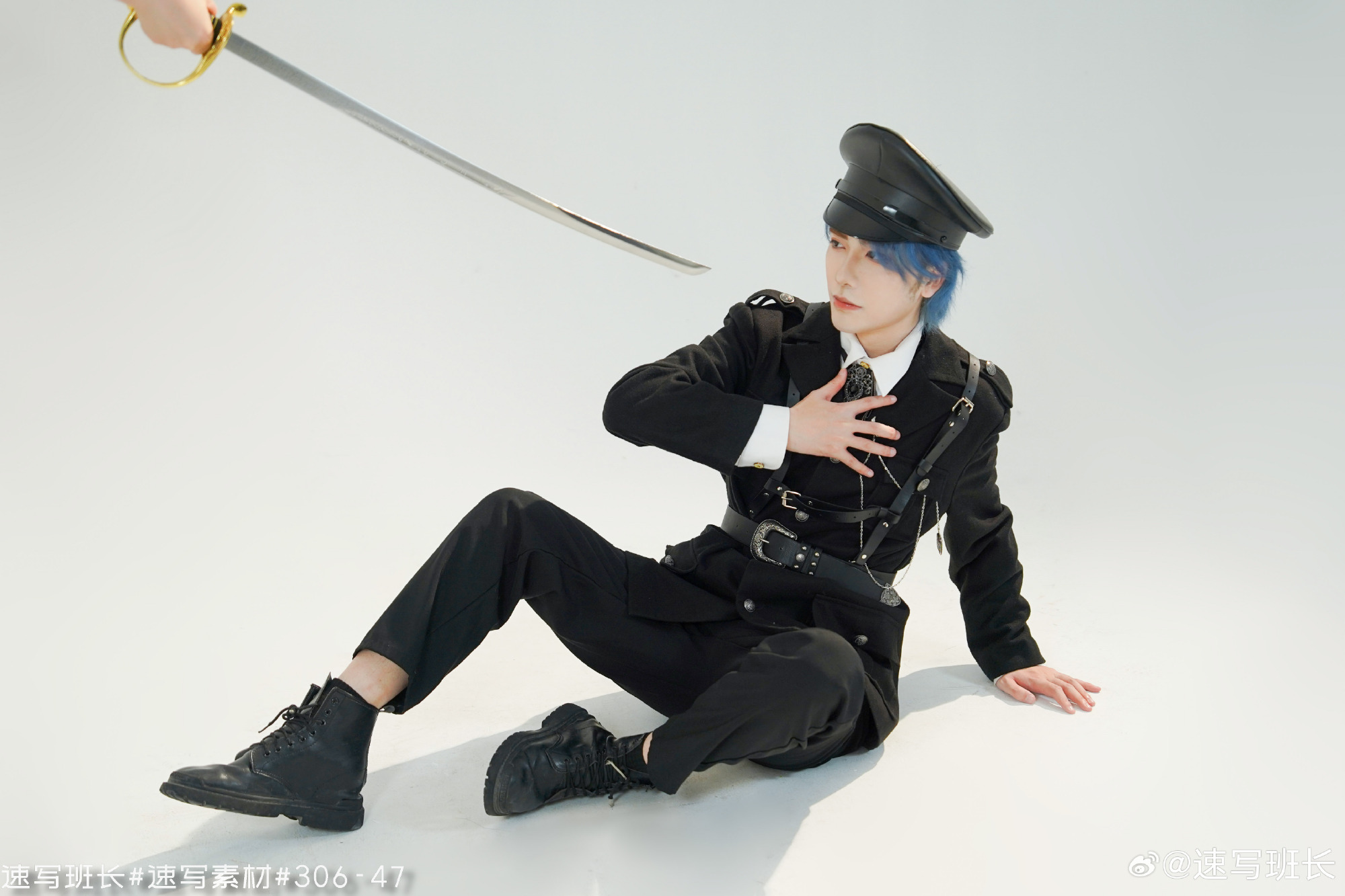 a young man with blue hair, dressed in a black militaryinspired uniform with silver accents, sits on a white floor.  he is dramatically posed with his hand on his chest, as if reacting to a sword being pointed at him from offscreen.  the lighting is bright and artificial, characteristic of a studio photoshoot.
