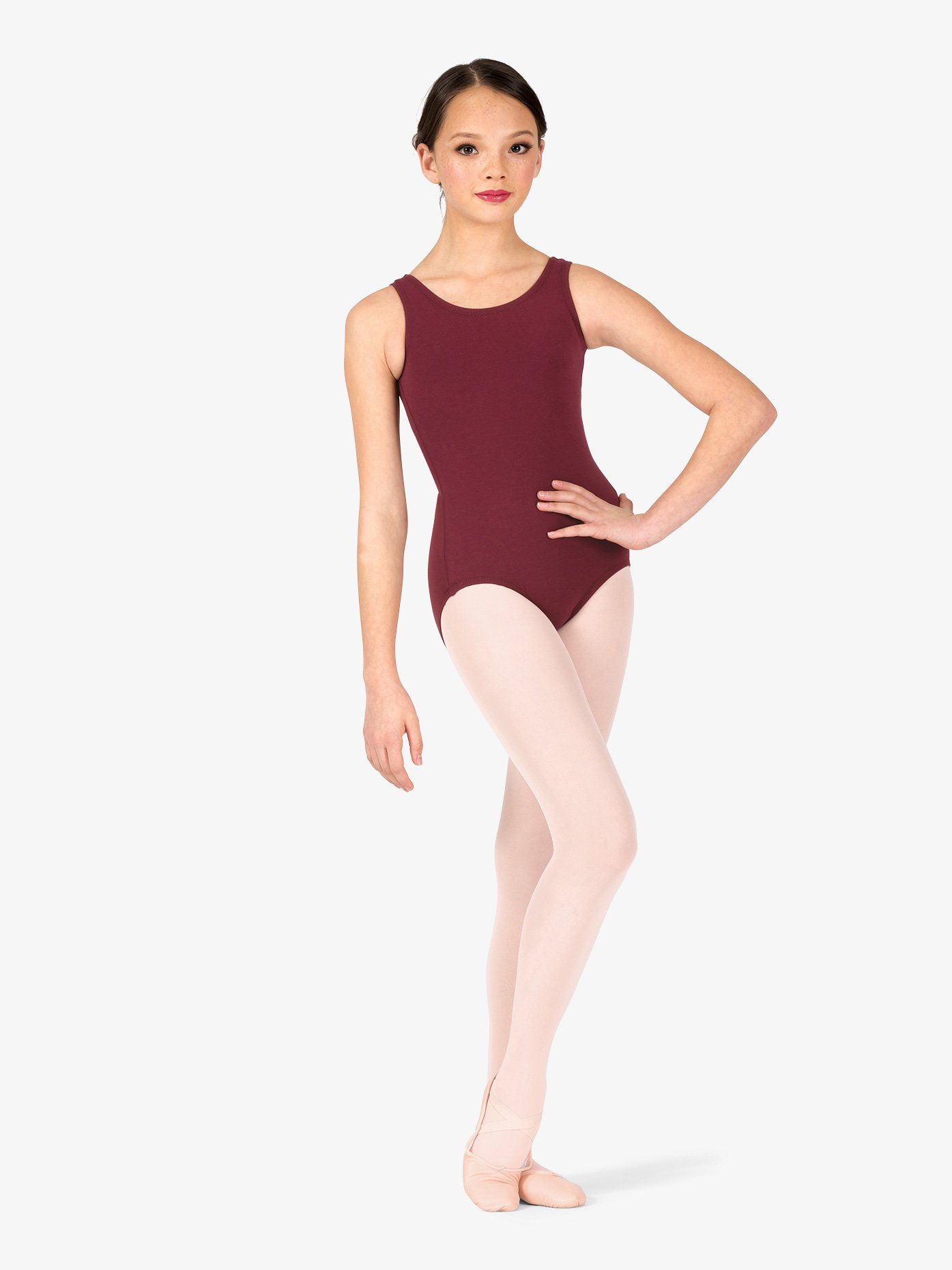 the image shows a young girl, possibly preteen or early teen, wearing a maroon/burgundy sleeveless ballet leotard and pink tights. she is standing in a ballet pose with her legs slightly apart and her hand on her hip.  she's wearing pink ballet shoes and has her hair neatly pulled back.  the background is plain white, providing a clean and simple backdrop that focuses attention on the dancer and her attire. the overall impression is one of grace and poise, typical of a ballet dancer's posture.