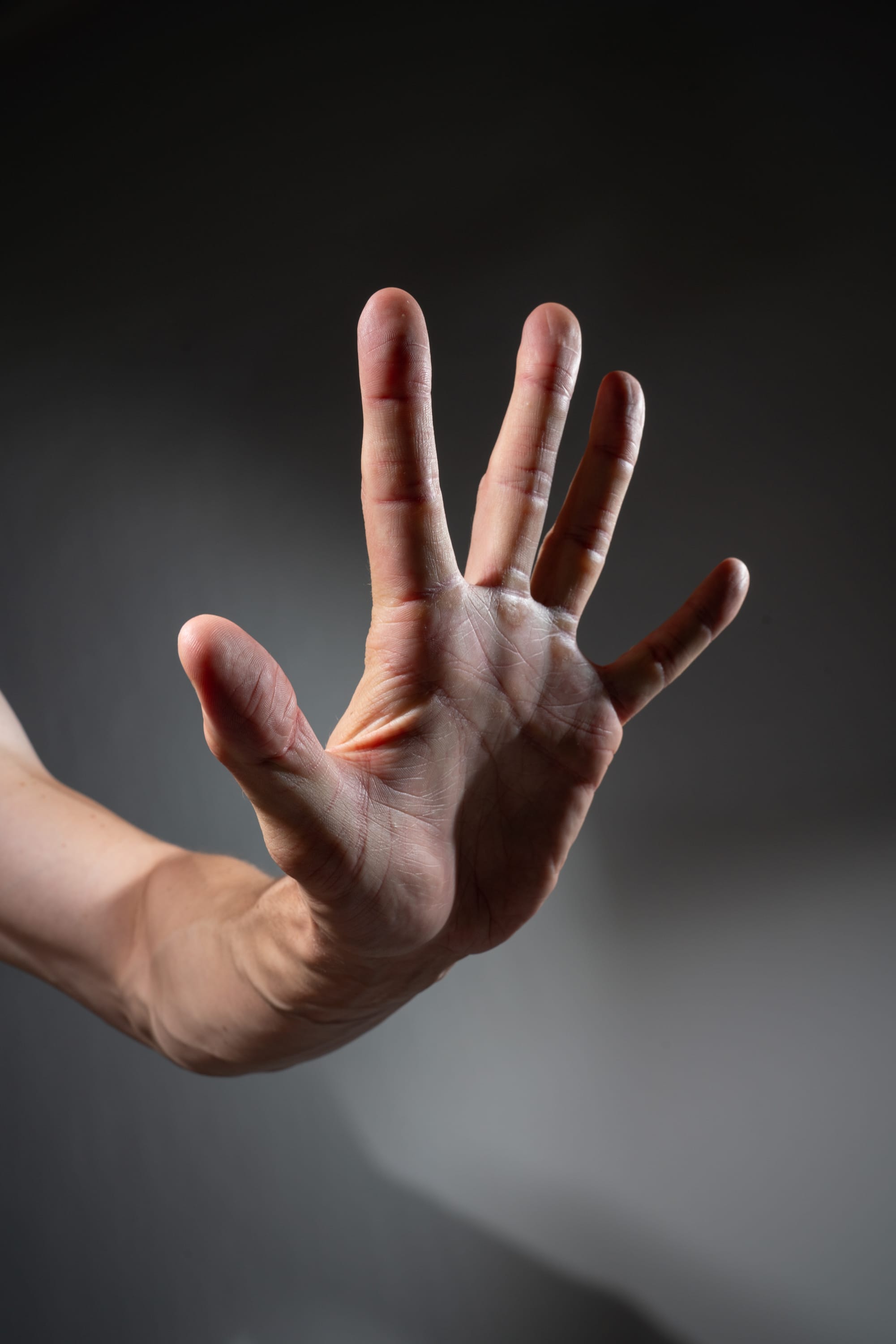 a man's hand is extended forward, palm facing out, in a gesture that universally signifies "stop." the hand is welllit against a dark background, highlighting the details and strength of the gesture.  the lighting creates a dramatic mood and emphasizes the importance of the message being conveyed.