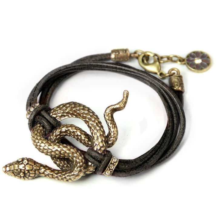a closeup shot of a snake bracelet featuring a goldtoned snake coiled around a multistrand leather band. the bracelet has a gold clasp and a decorative charm.