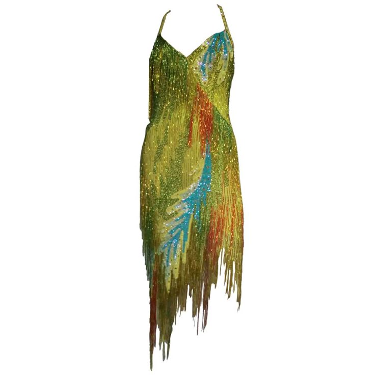 a sequined cocktail dress with spaghetti straps and an asymmetric hem is presented on a white background. the dress is predominantly green and yellow, with areas of red and blue. it has a sleeveless design and an asymmetrical hemline with fringe detailing.