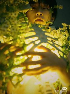 a portrait of a young man holding a neonlit ribcage skeleton intertwined with white flowers in front of him, partially obscuring his face. the image is predominantly lit with yellow neon light, creating a stark contrast between light and shadow and highlighting the skeletal structure.