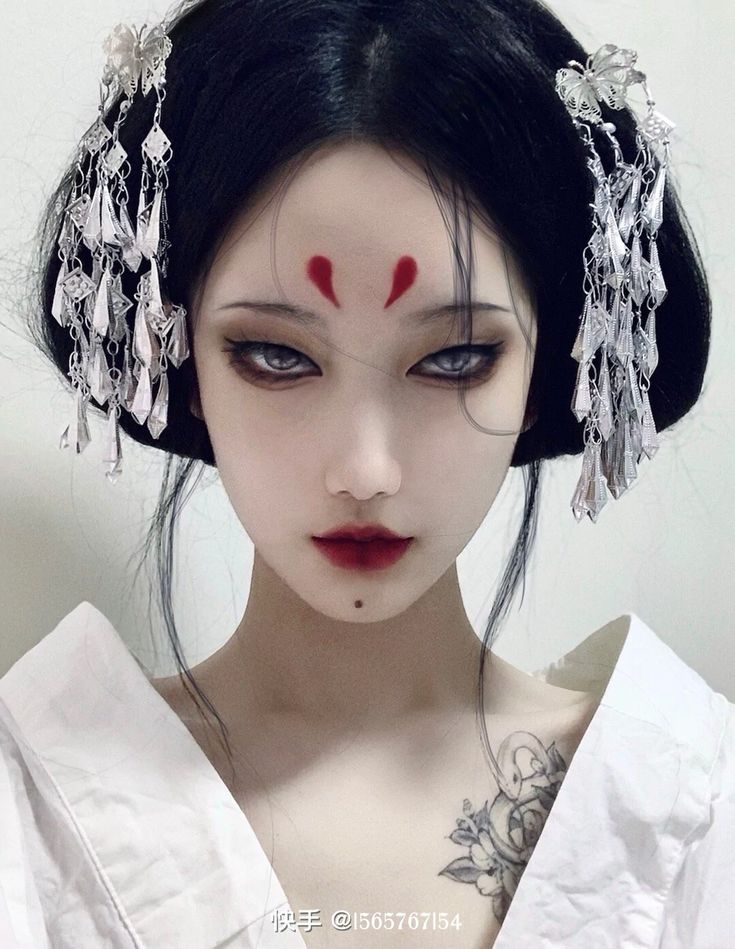 a young asian woman poses for a portrait against a neutral background. she is wearing elaborate silver hair ornaments and dramatic makeup that includes winged eyeliner, bold red lipstick, and a red forehead design. her expression is serious and her gaze is direct at the viewer. she is wearing a white garment that covers her shoulders and chest.  the image has a highfashion, editorial feel with a nod to traditional chinese aesthetics.