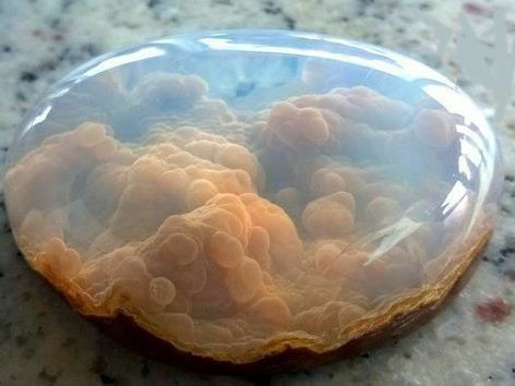 a closeup image of a polished agate gemstone. the agate is translucent, showing a beautiful pattern of brown and white swirls and bubbles. it looks like a miniature landscape or a celestial nebula. the agate has a smooth surface, reflecting light in various colors.  the image showcases the intricate beauty of nature's artistry in the form of a mineral.