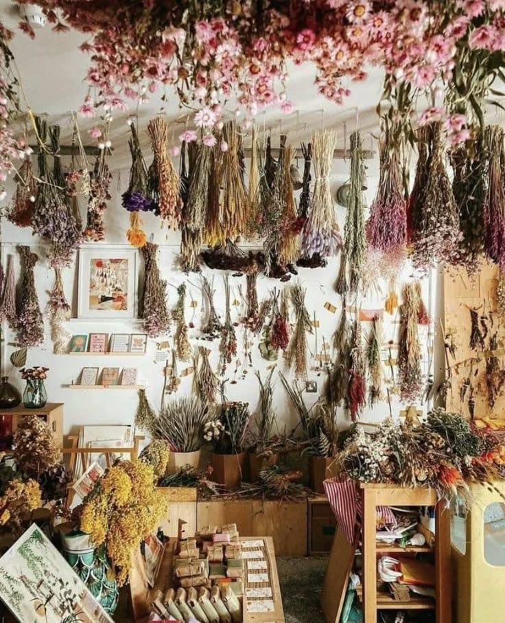 the image shows the interior of a flower shop filled with an abundance of dried flowers. bunches of flowers are hanging from the ceiling, creating a dense overhead display. more dried flowers are arranged on shelves and tables. the scene suggests a retail environment with a focus on floral arrangements, design, and possibly crafting or art.
