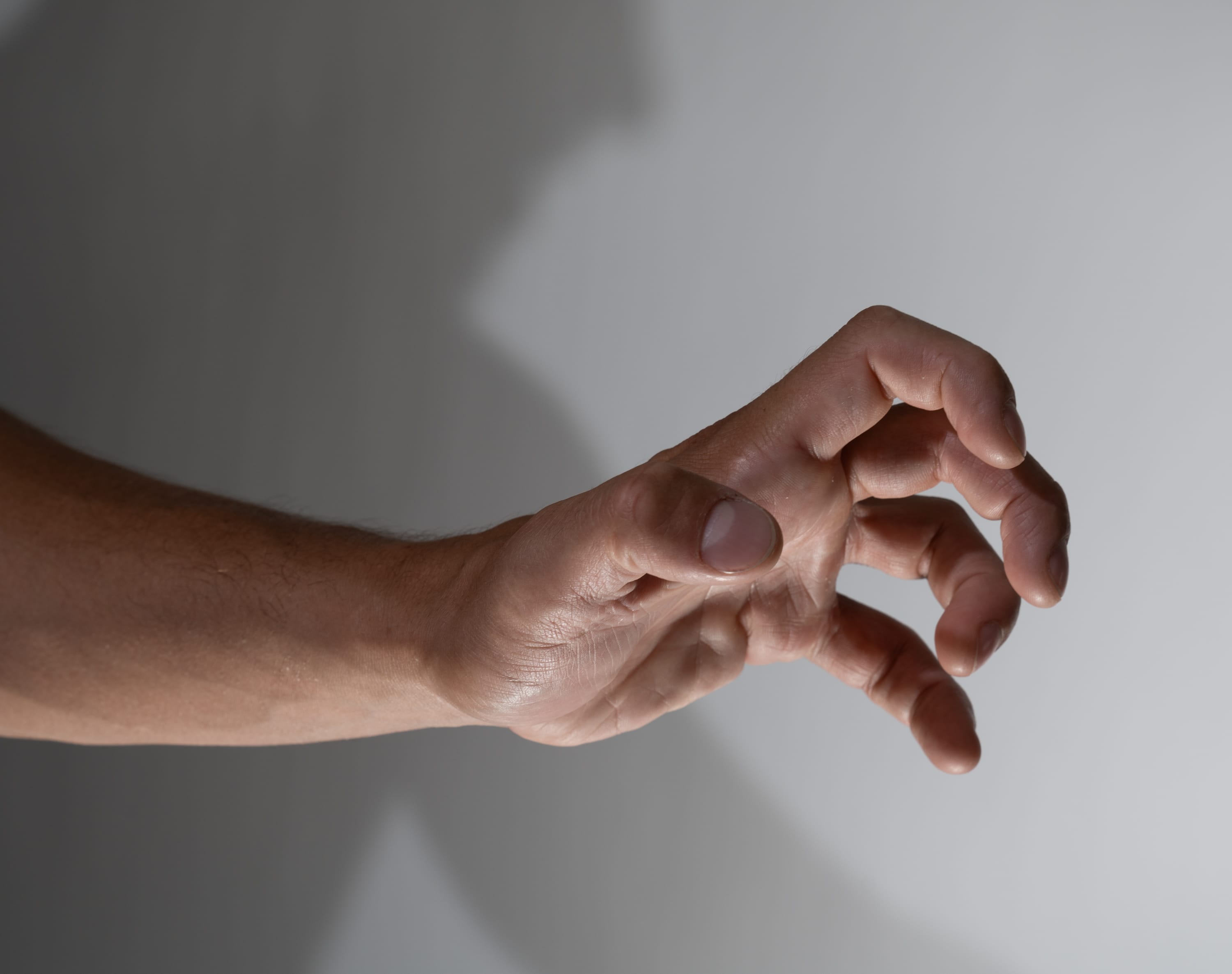 a closeup image of a man’s arm and hand reaching forward. the hand is in a clawlike gesture as if it is reaching to grab something. the image is lit with studio lighting and uses a plain background.