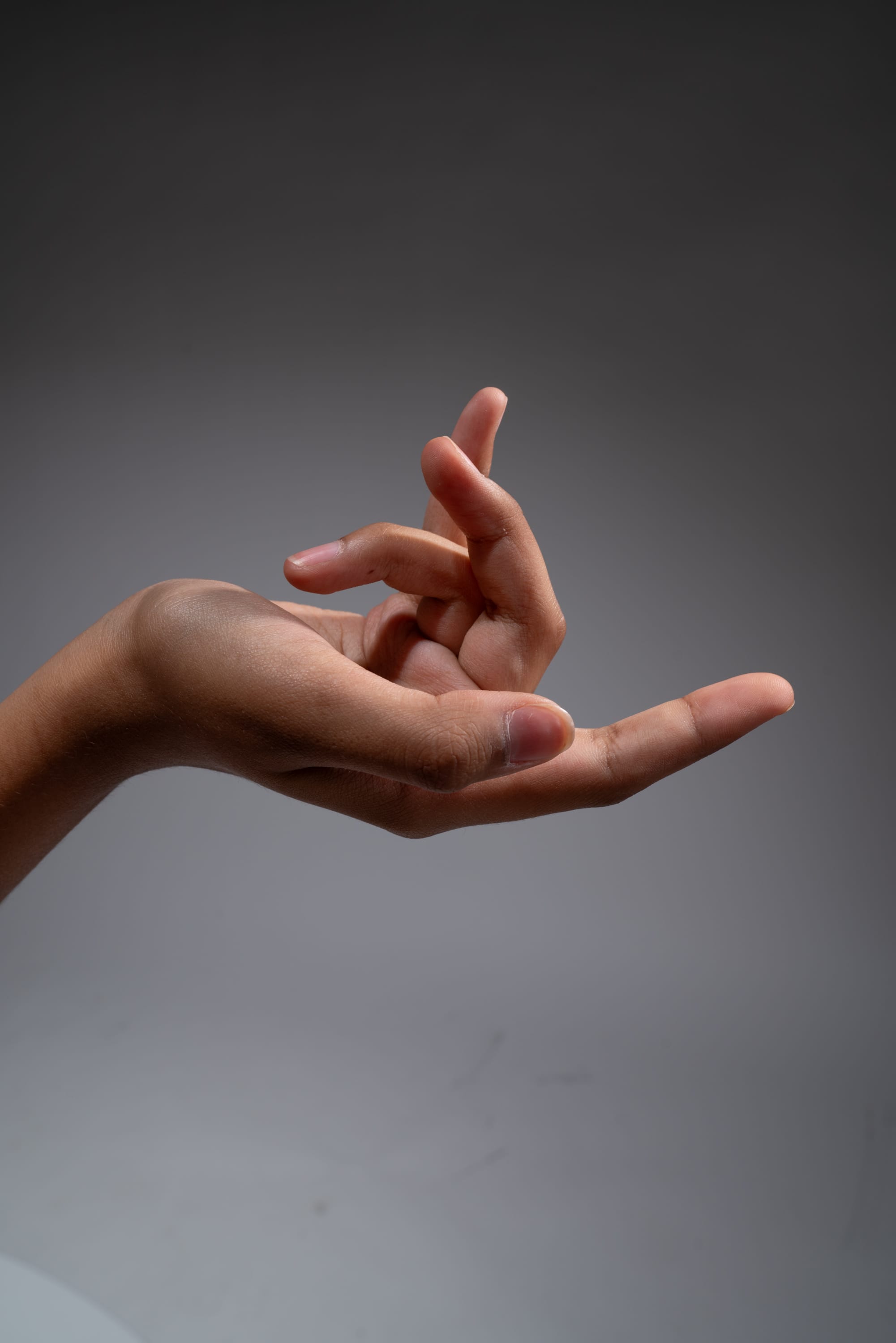 a hand is posed against a gray background, forming a mudra with the fingers. the lighting is soft and natural, highlighting the contours of the hand.