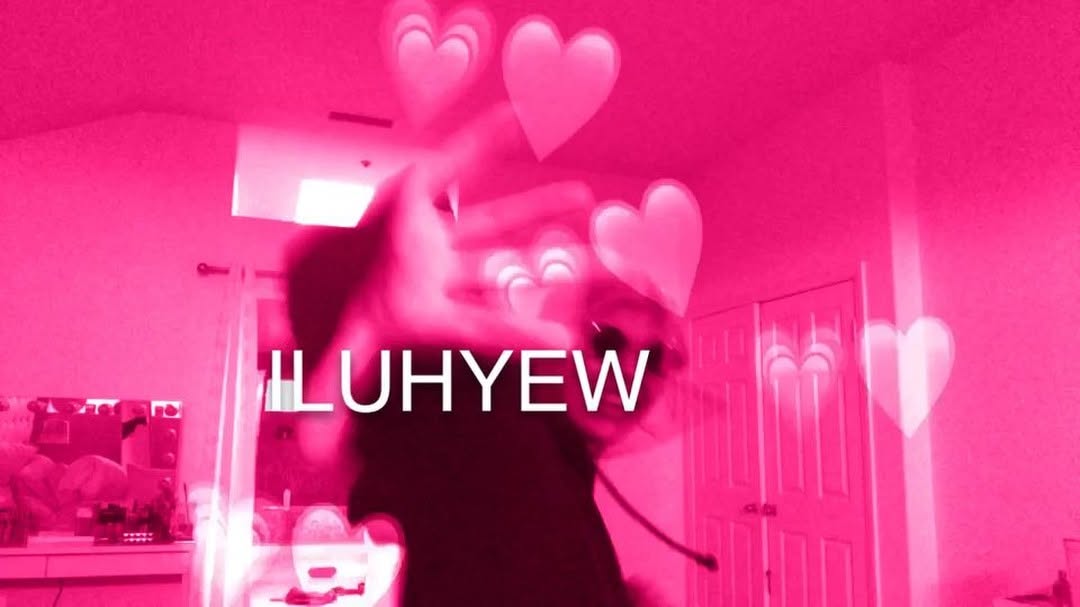 a blurry pinkfiltered image shows a person with their hand raised, and floating heart graphics. the text "iluhyew" is overlaid. the background shows a room interior with doors and furniture.
