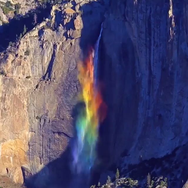 an aerial view of a majestic waterfall cascading down a towering cliff face in yosemite national park. the water is misting as it falls, creating a rainbow that stretches along the cliff. the sunlight shines through the mist, illuminating the colors of the rainbow. the scene is one of incredible natural beauty, showcasing the power of nature.