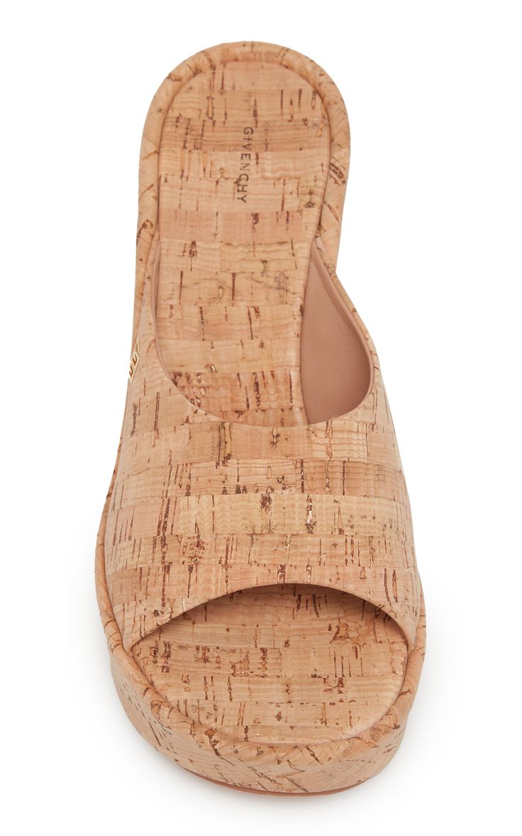 a closeup, topdown shot of a pair of givenchy women's cork wedge sandals. the sandals are beige and have an opentoe design with a platform wedge heel. the cork material has a visible textured pattern. the givenchy logo is subtly imprinted on the insole. the image is welllit and provides a clear view of the shoe's details.