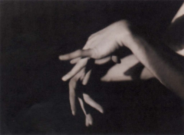 the image is a black and white photograph of a woman's hands. the hands are positioned in a way that suggests movement or gesture. the background is dark and out of focus, drawing attention to the hands. the image has a surreal and abstract quality, evoking a sense of mystery and emotion. the overall tone is dark and moody.