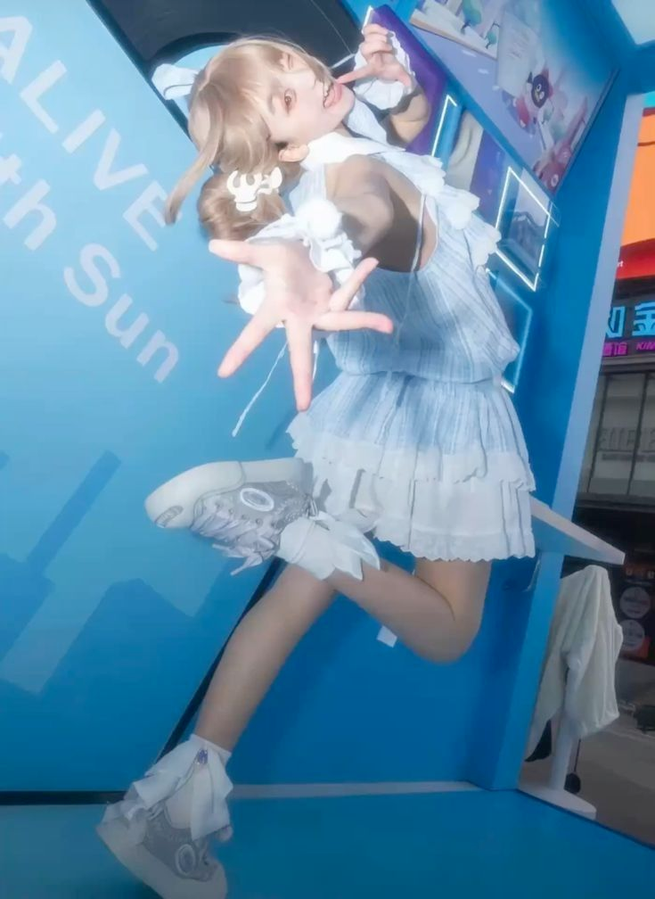 a young woman in a light blue dress and white sneakers jumps playfully in an urban setting against a backdrop of vibrant blue advertising signage. her pose is dynamic, captured from a low angle that emphasizes her energy and the colorful environment. the overall mood is cheerful and lively.