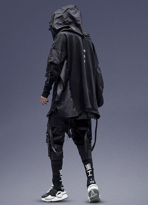 a man is wearing a black hoodie and matching black pants with white and black sneakers. he is posing in front of a grey background. his outfit is considered streetwear fashion.