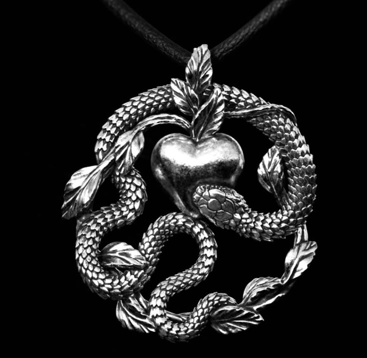 a black and white photograph shows a silver pendant depicting a snake coiled around an apple with leaves. the pendant is suspended from a black cord or necklace.